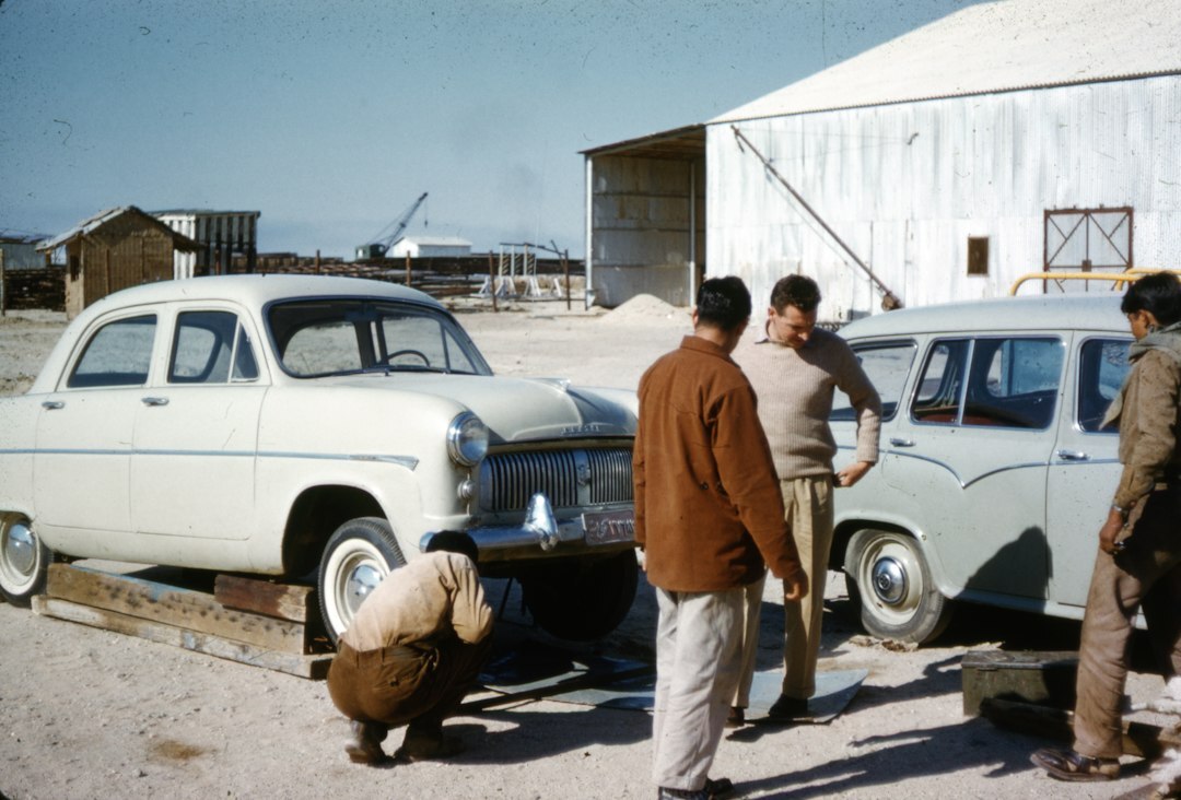 Editorial team reviewing archive photographs of classic automobiles at a wooden desk